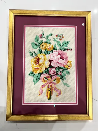 Floral needlework in a gold frame with burgundy double matting.