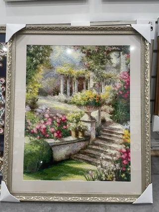 Garden scene needlework in an ornate silver-coloured frame with a pale mat.