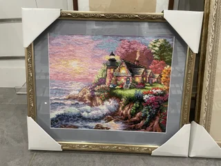Lighthouse needlework in an ornate gold-coloured frame with a grey mat.